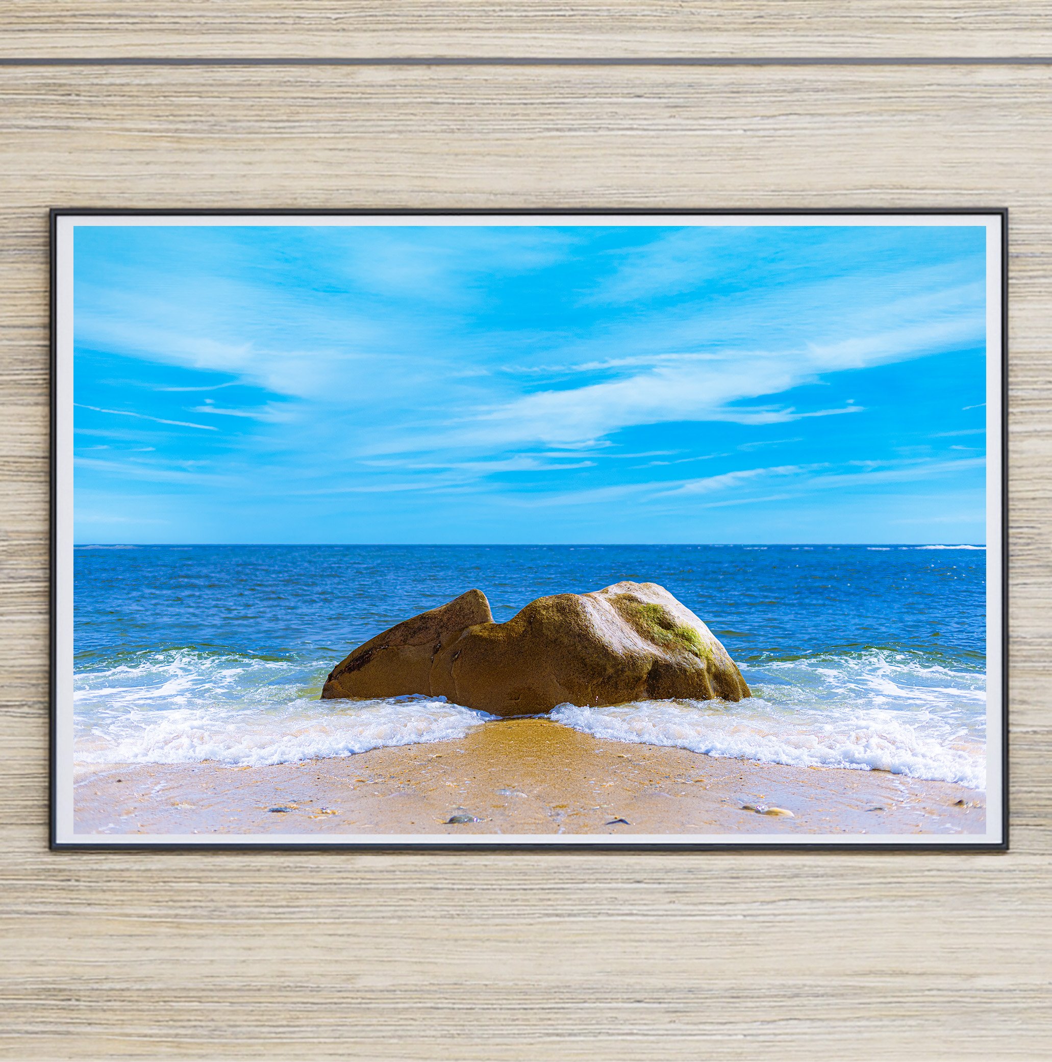 Fine art photograph of a large golden-brown boulder surrounded by white Atlantic waves on a sandy Long Island beach beneath a vivid blue sky.
