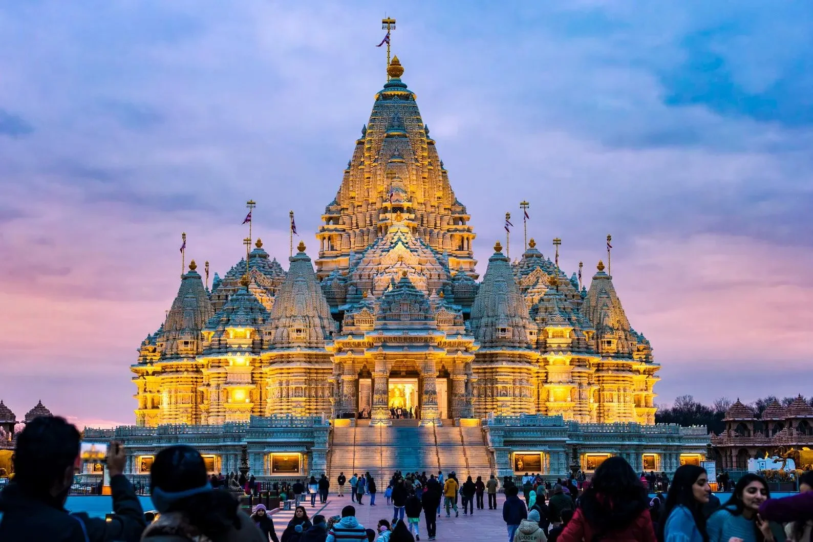 Fine art photograph of BAPS Swaminarayan Akshardham in Robbinsville, New Jersey, warmly illuminated at sunset beneath a pastel blue, pink, and lavender evening sky.