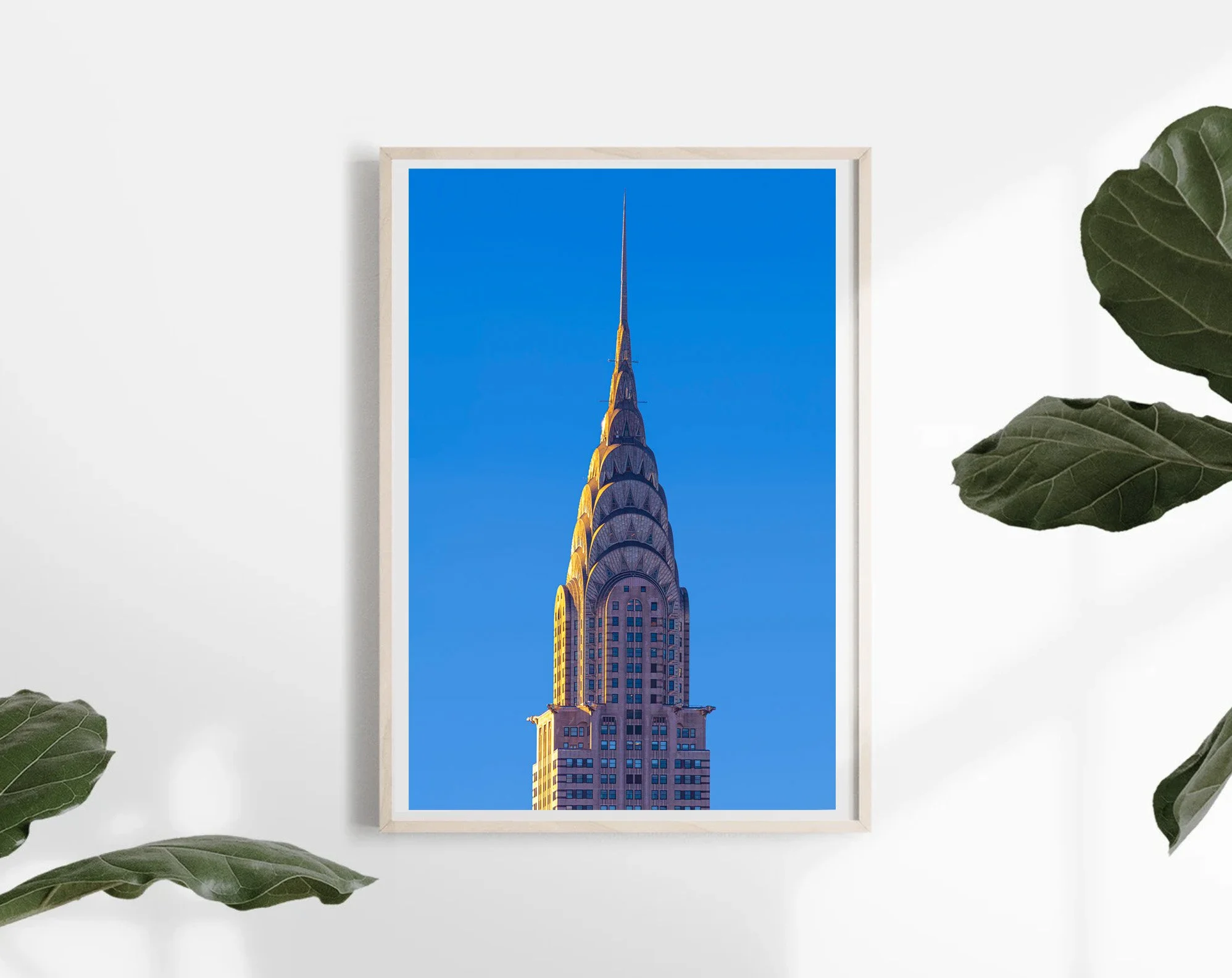 Vertical photograph of the Chrysler Building's iconic Art Deco crown and pointed spire, illuminated by warm sunlight against a vivid blue New York City sky.