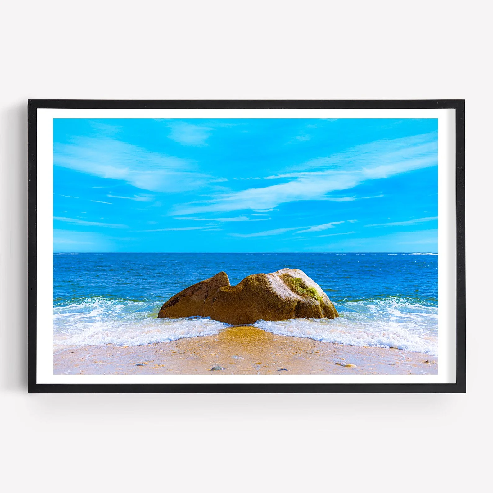 Fine art photograph of a large golden-brown boulder surrounded by white Atlantic waves on a sandy Long Island beach beneath a vivid blue sky.