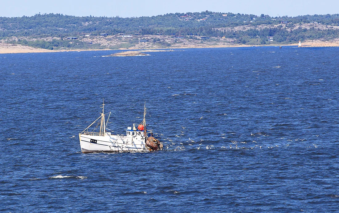 Fiskebåt med hyttefelt på Spjærøy og Kirkøy i bakgrunn + Pikesten fyr på Asmaløy.