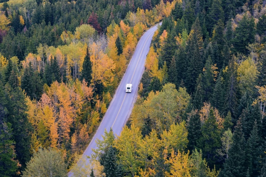 Aerial view of two-lane highway cutting through forest with RV driving on it