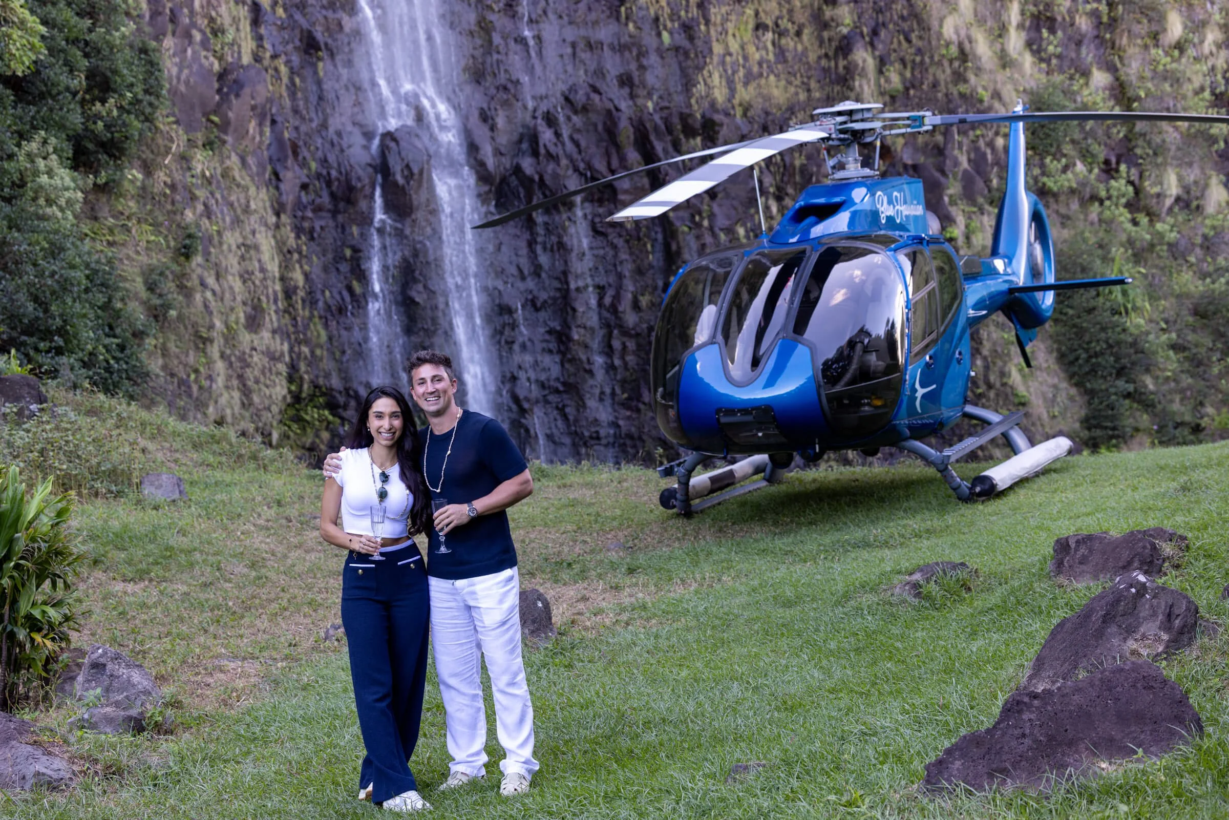 Couple cerebrating their proposal in front of a waterfall they flew to by helicopter