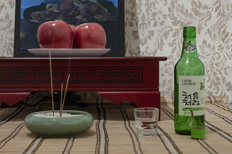 Mom, I can get married now! Installation: performance documentation, apple soju, soju glass, incense, rice, incense holder, apples, ceramic plate, bamboo curtain, 밥상, wallpaper. Installation view.