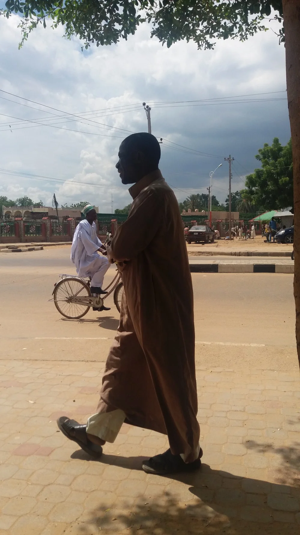 Man walking, dressed in Jalabia and another on Bike dressed in Agbada/Babaringa