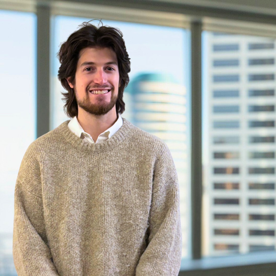 Photo of Josh Savitz standing in front of windows with blurred office towers in the background.