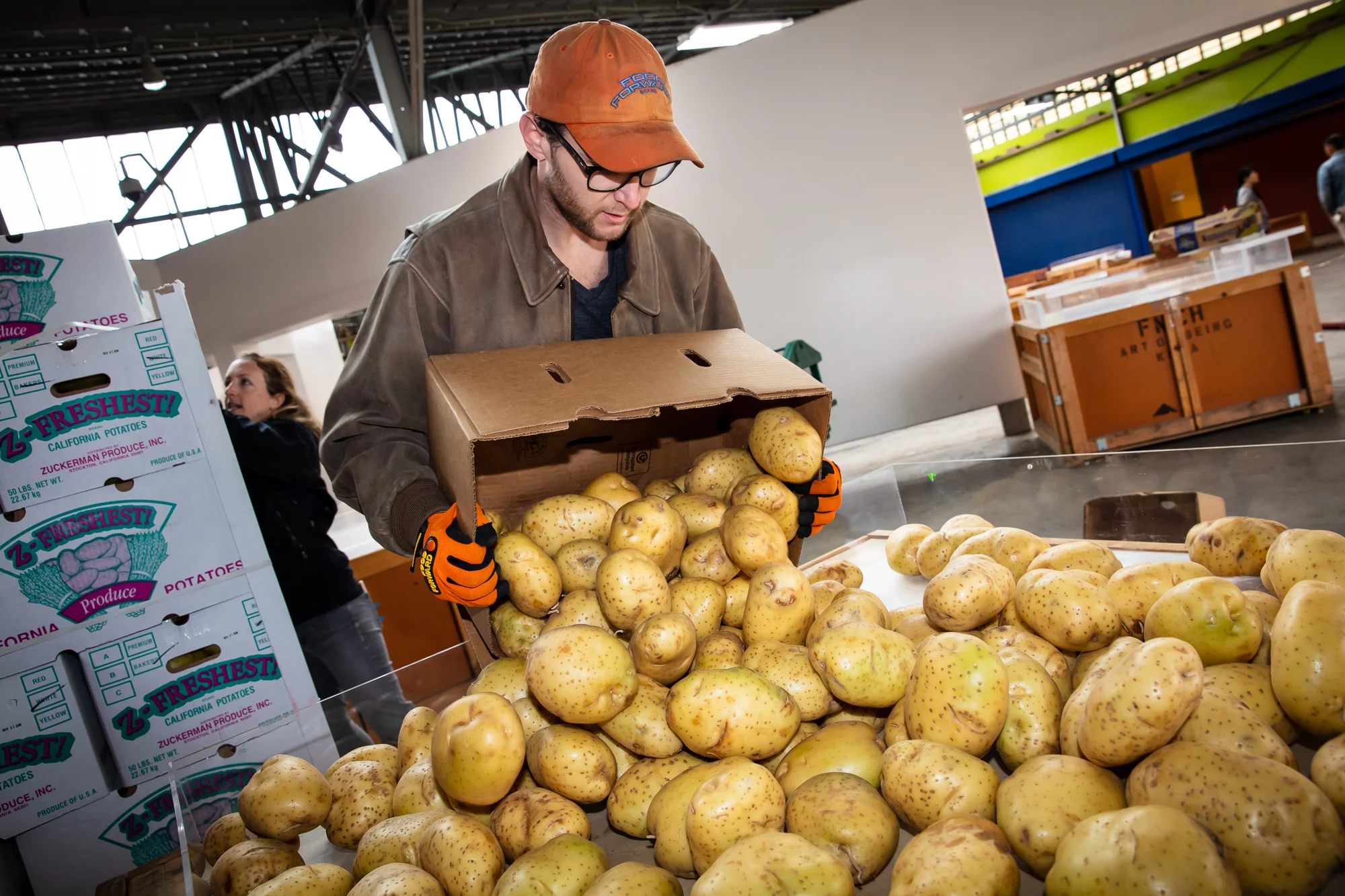 Food waste prevention and rescue grant program, california climate investments. image depicts a man dumping a box of potatoes into a large CONTAINER, filled with potatoes.