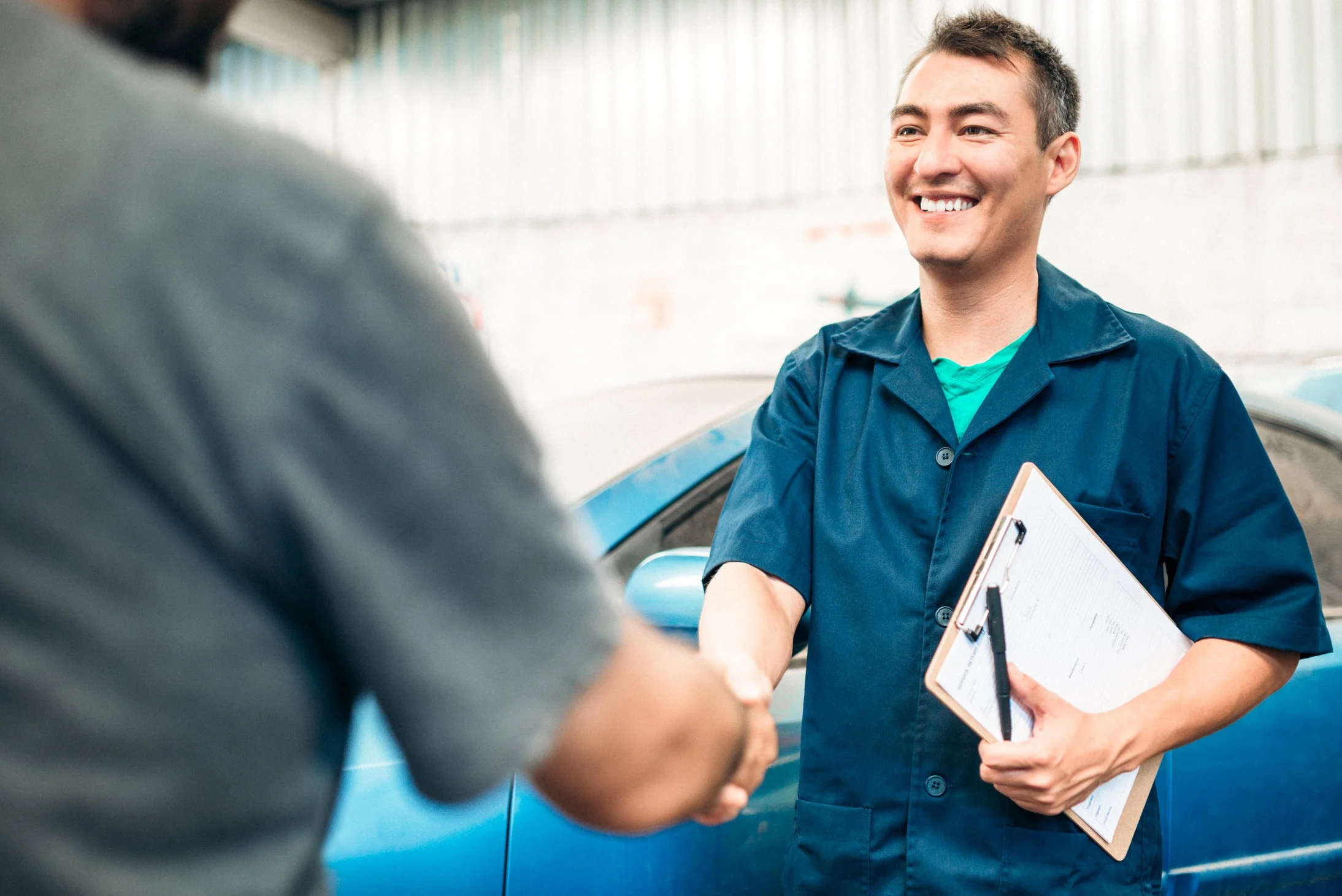 clean cars for all, california climate investments. the image depicts a man holding a clipboard, standing in front of a car, shaking another man’s hand.