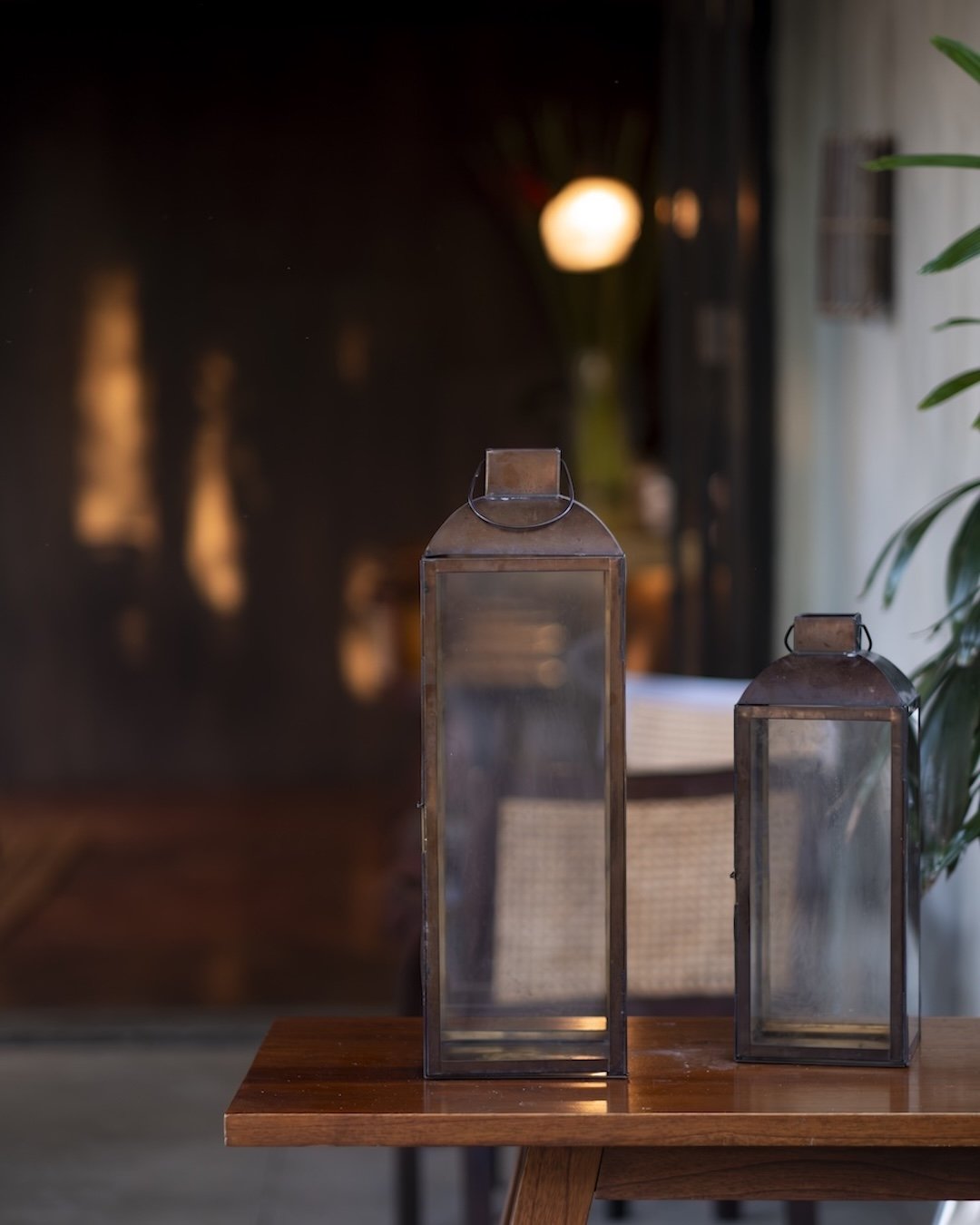 Copper Bar Ubud's two vintage glass lanterns with metal frames on a wooden table in a dimly lit room.