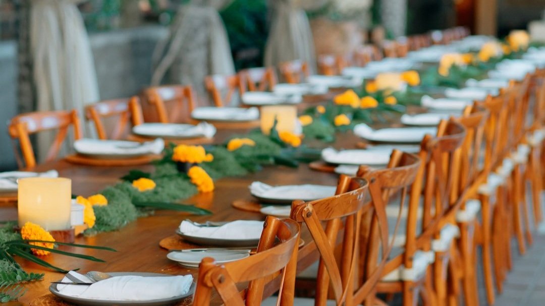 Long dining table set with white plates, yellow flowers, and wooden chairs.