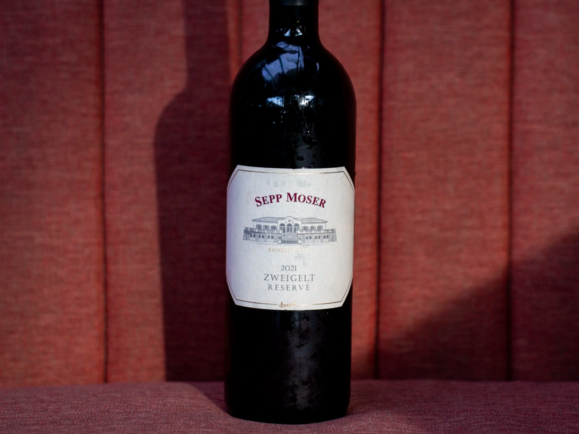 A dark wine bottle with a white label is one of copper wines, placed against a red textured background.