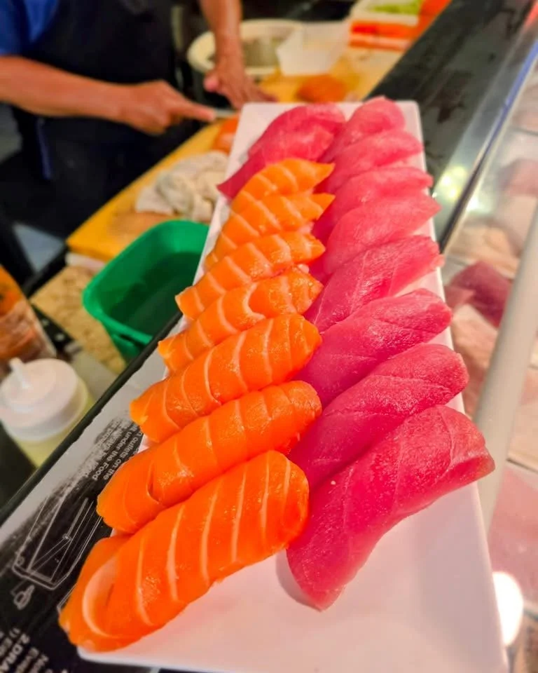 Sashimi set with sliced salmon and tuna arranged on a white platter at a sushi bar.