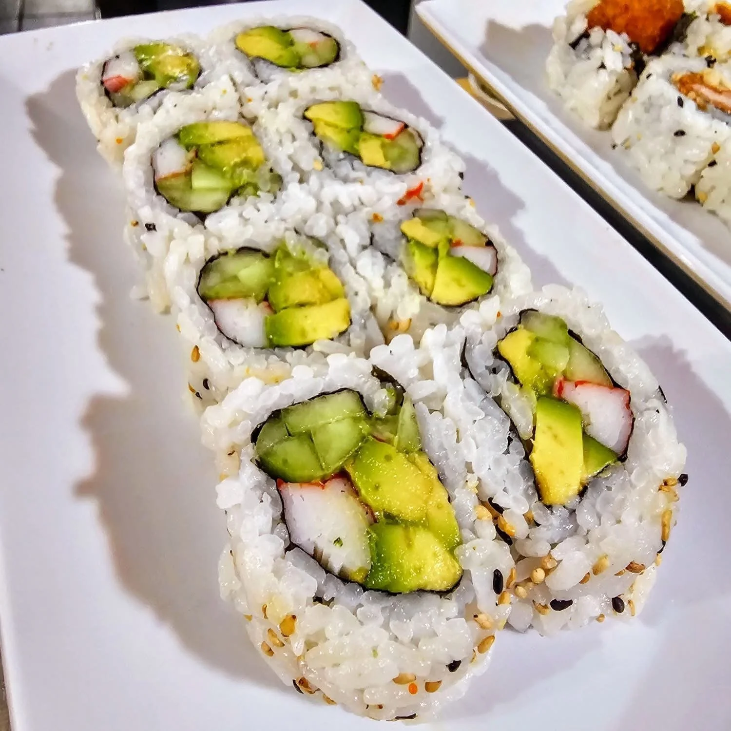 Close-up of a plate of vegetable sushi rolls with cucumber and imitation crab on a white rectangular plate.
