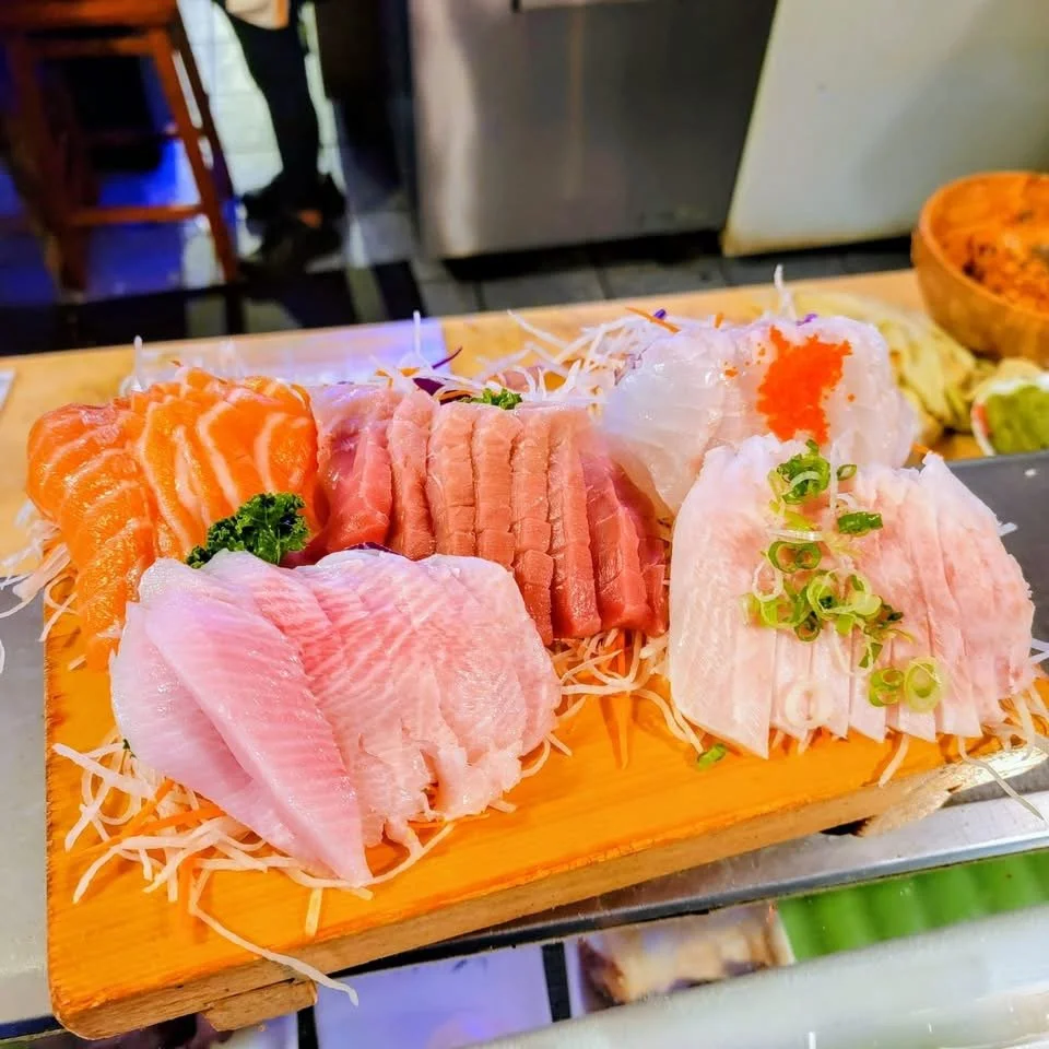 Assorted slices of raw fish sashimi on a wooden platter, garnished with green onions and shredded daikon, served on a bed of shredded daikon radish.
