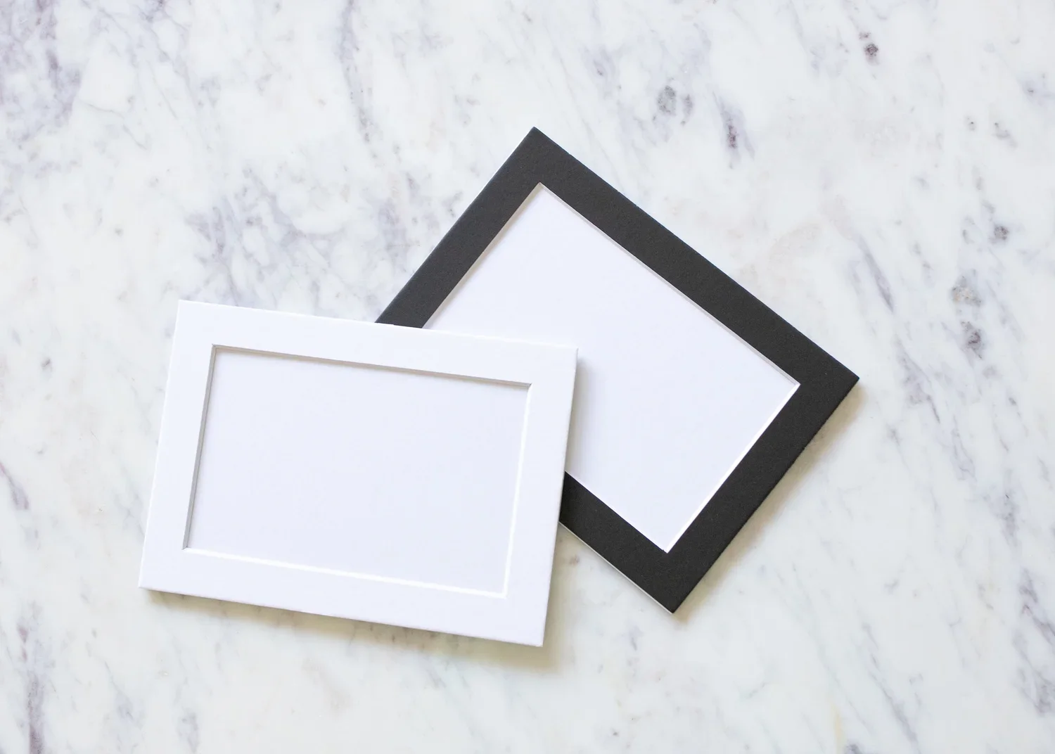 Two blank picture frames, one white and one black, placed on a white marble surface.
