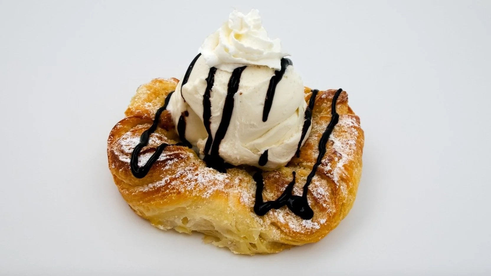 Dessert with a fried pastry topped with whipped cream, chocolate syrup, and dusted with powdered sugar.