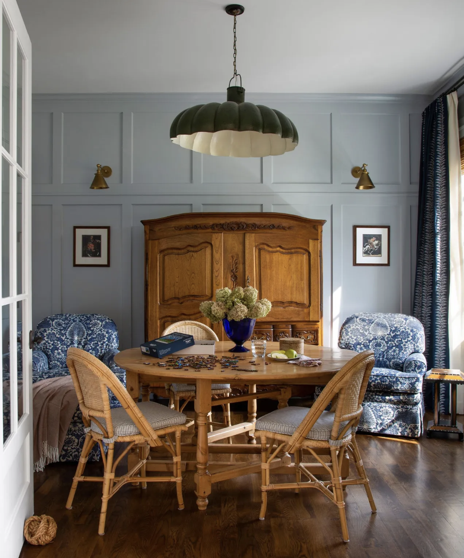 Charming puzzle room by Nadia Watts Interior Design featuring a vintage armoire, blue patterned armchairs, and a wooden table with a puzzle in progress.