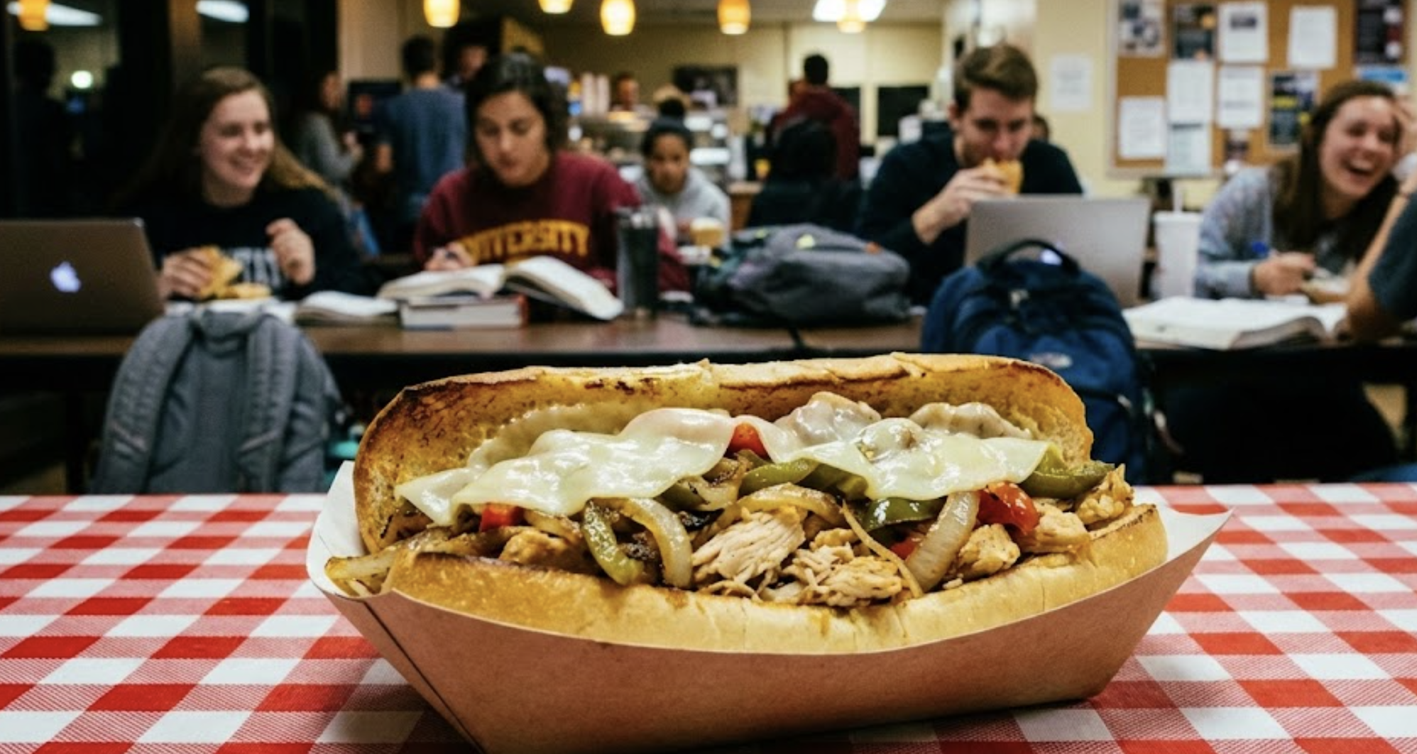 AI generated image of a chicken cheesesteak sandwich with a blurry background of students studying in a college food hall.