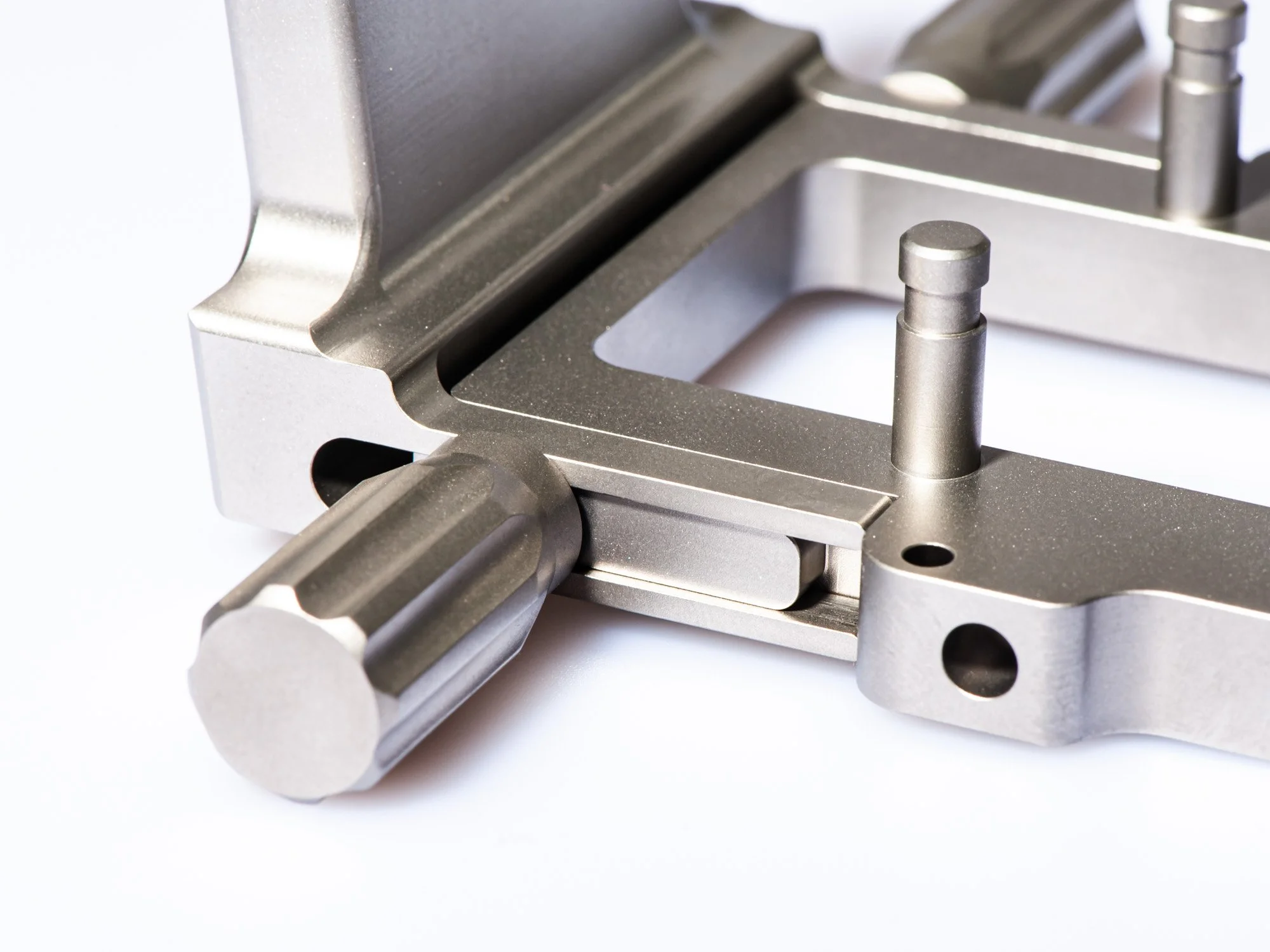Nahaufnahme eines metallischen Maschinenbauteils mit verschiedenen Schrauben und Bolzen auf weißem Hintergrund.