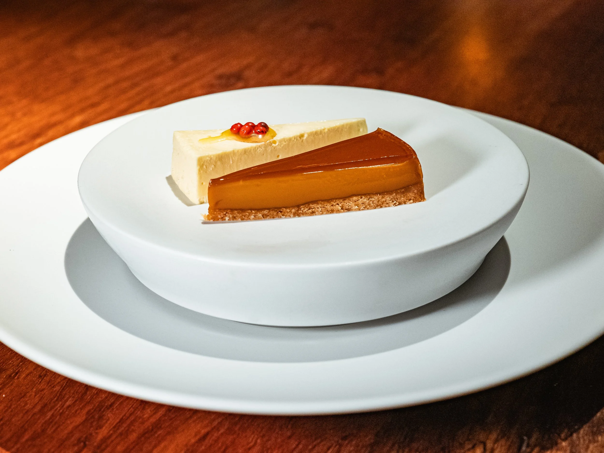 Zwei Tortenstücke auf einem weißen Teller, einer scheint Karamell und die andere ist cremig mit roten Beeren.