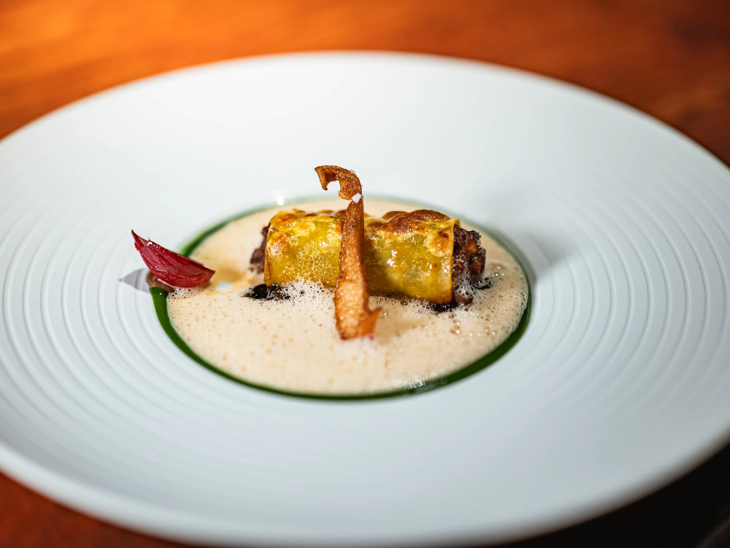 Feines Gericht mit Zartheit und bunten Akzenten, präsentiert auf einem weißen, konkaven Teller mit fein strukturiertem Rand.