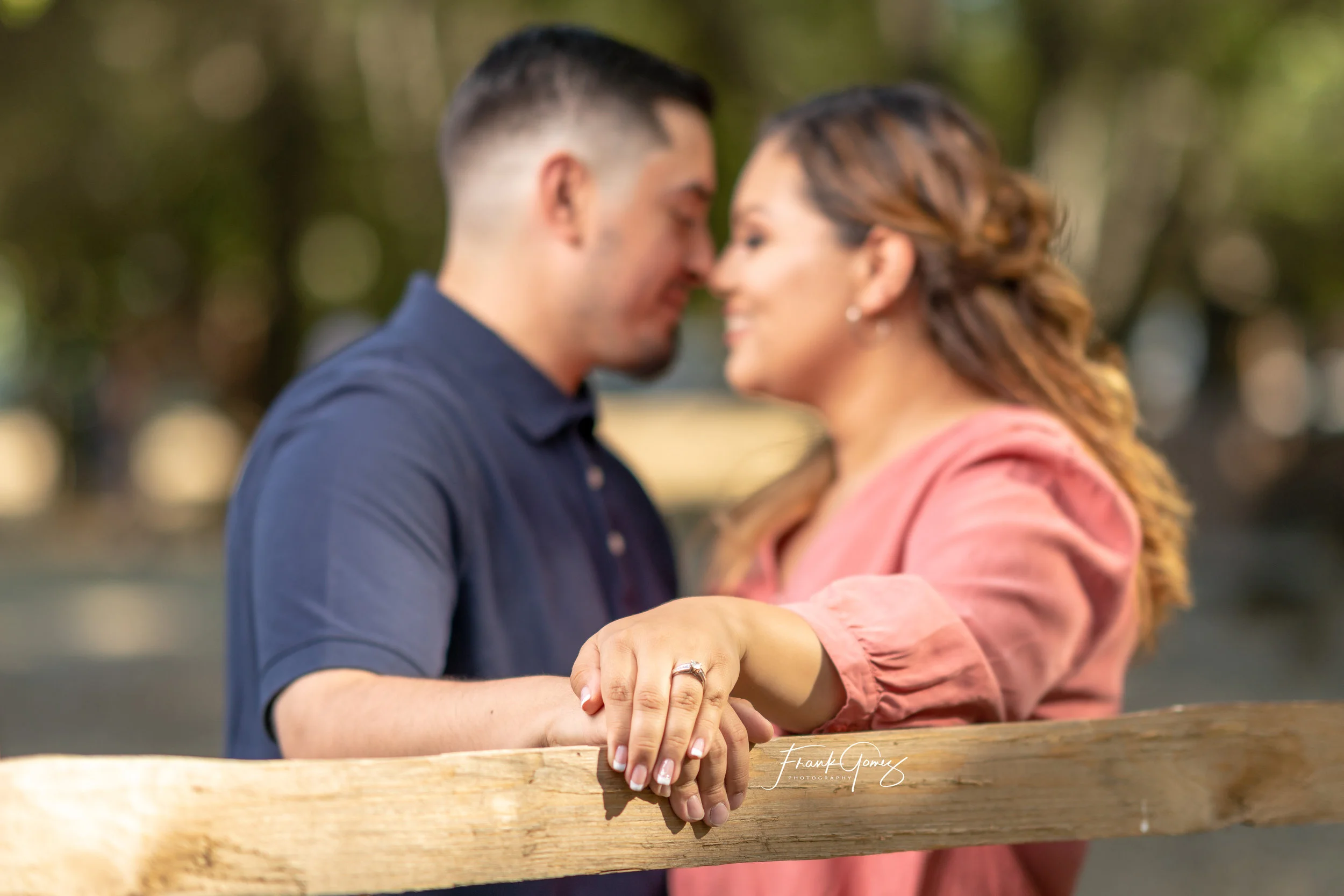 Outdoor Engagement Photo in park setting of couple by rustic fence featuring engagement ring