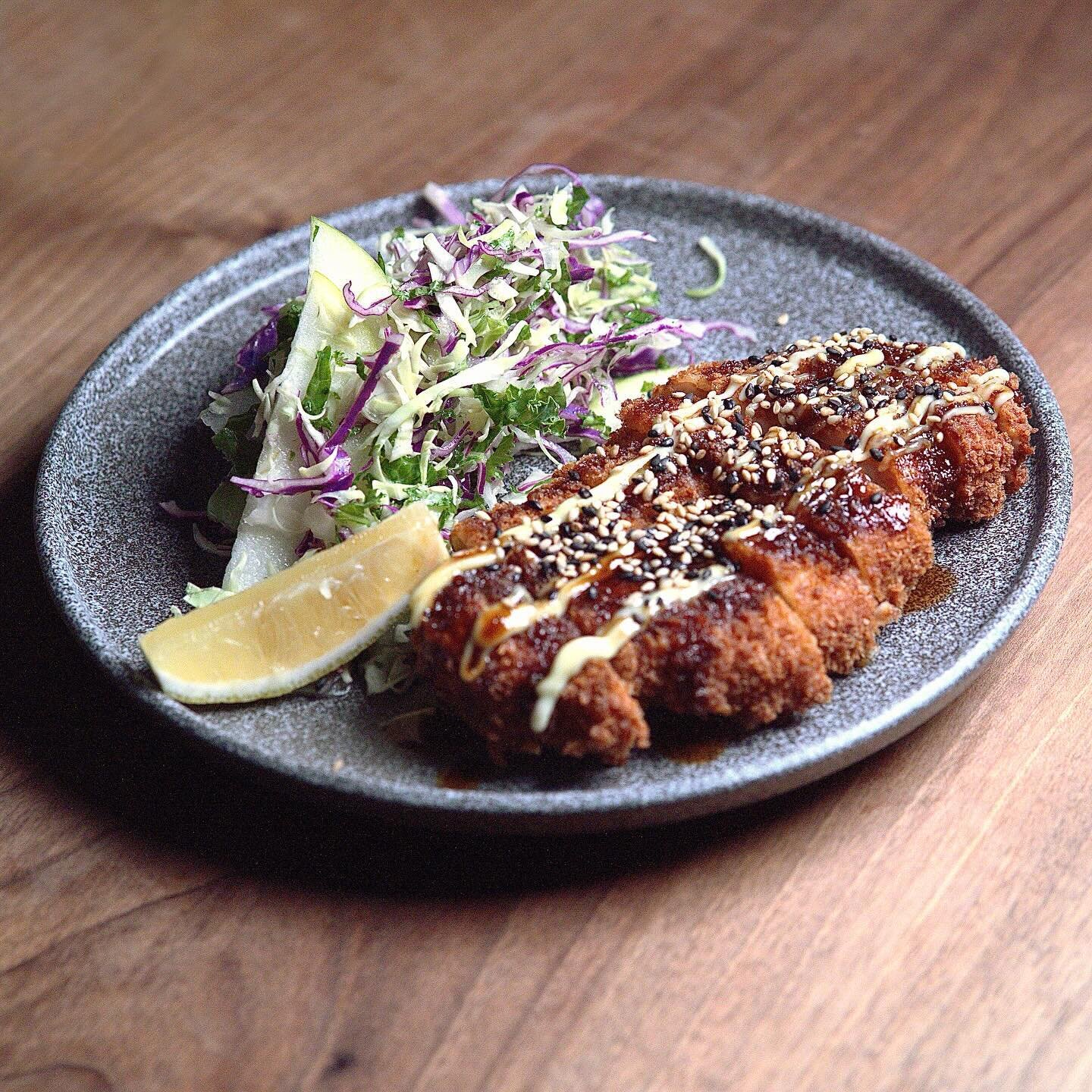 Our Tonkatsu is a Japanese schnitzel topped with black garlic teriyaki sauce, mayo and sesame seeds. A fresh kale salad on the side and hot karashi mustard.