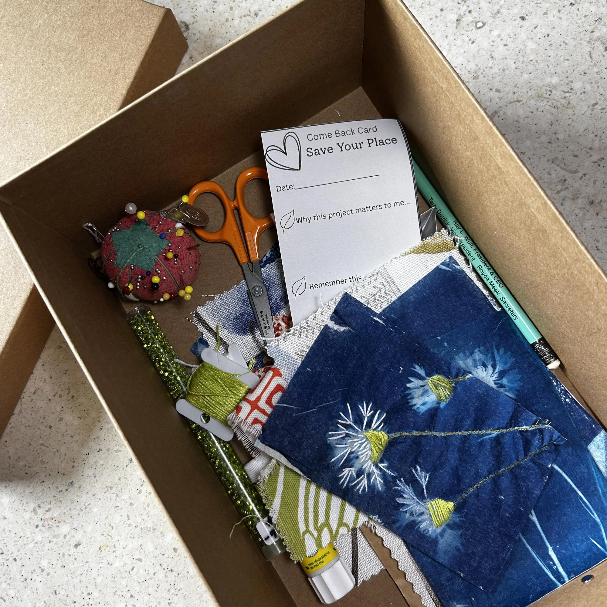 Open Come Back Box with scissors, embroidery floss, pincushion, fabrics, and unfinished textile art project.