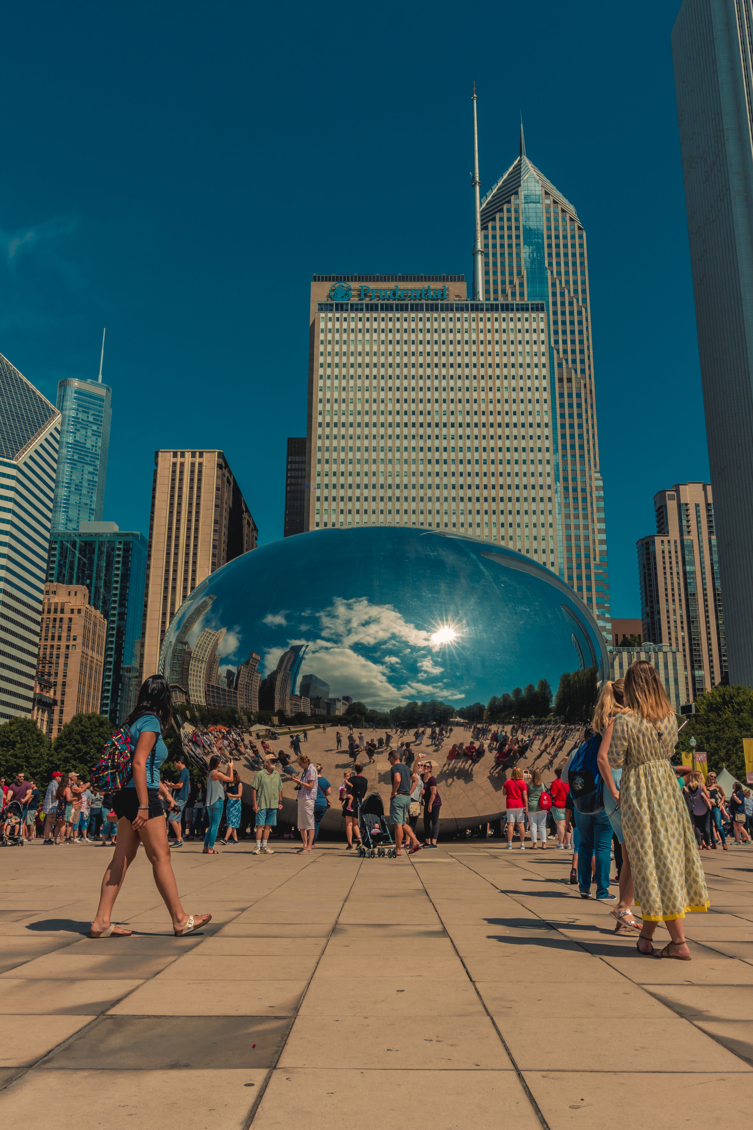 People gathered around and taking pictures of the Cloud Gate (The Bean) sculpture in Millennium Park, Chicago, with city skyscrapers reflected in its shiny surface.