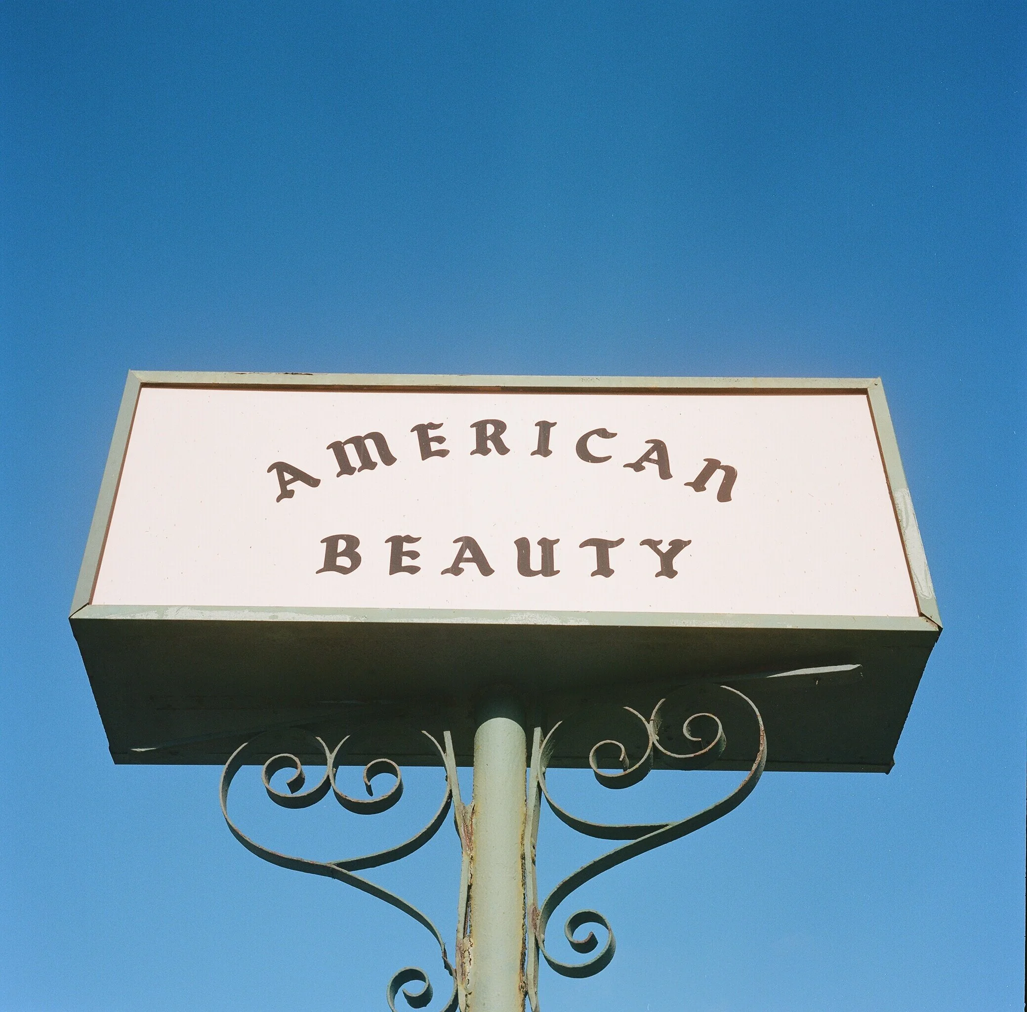 A sign with the words "American Beauty" against a clear blue sky.