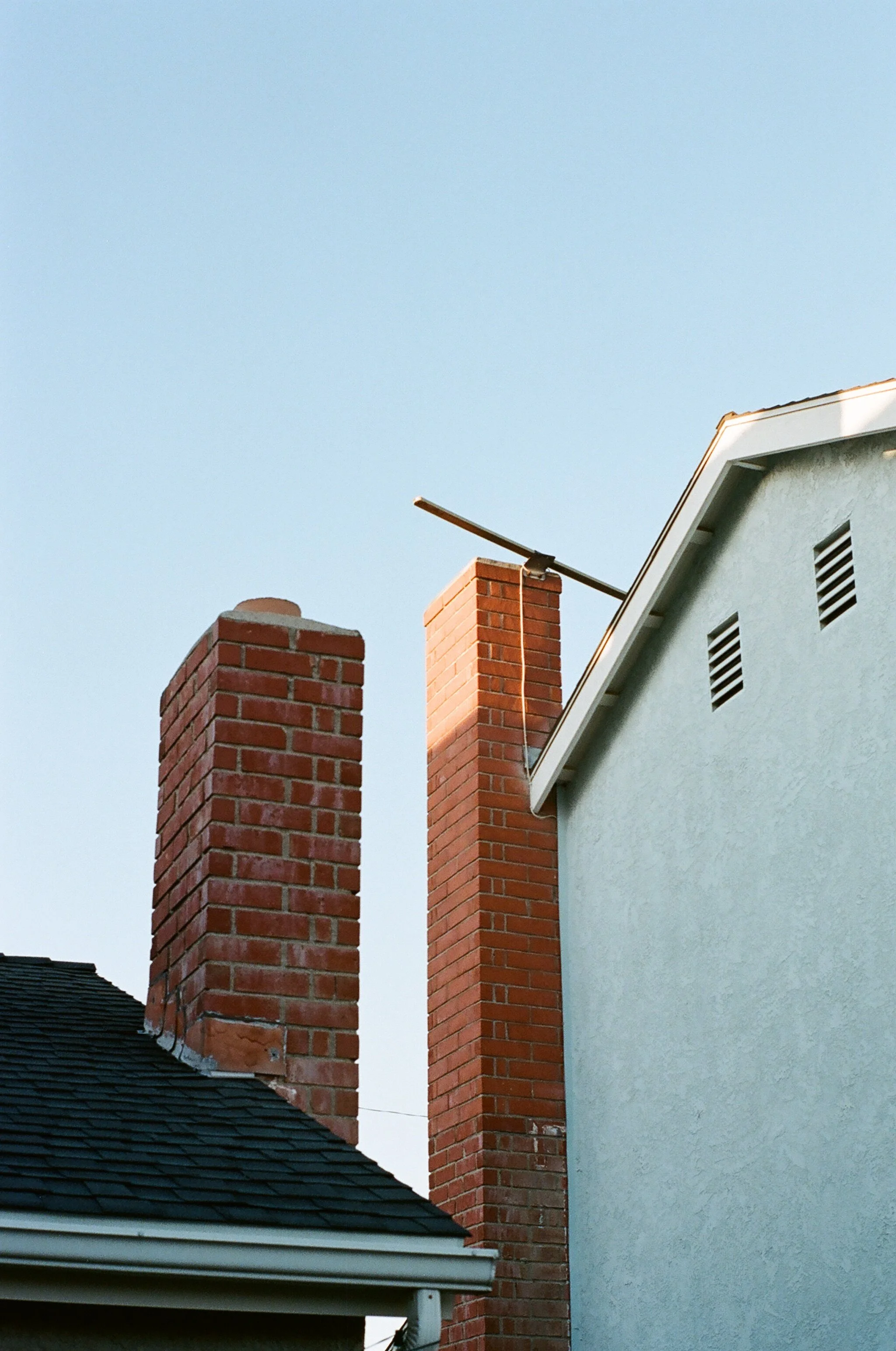 View of two brick chimneys on a house with a light blue sky background.