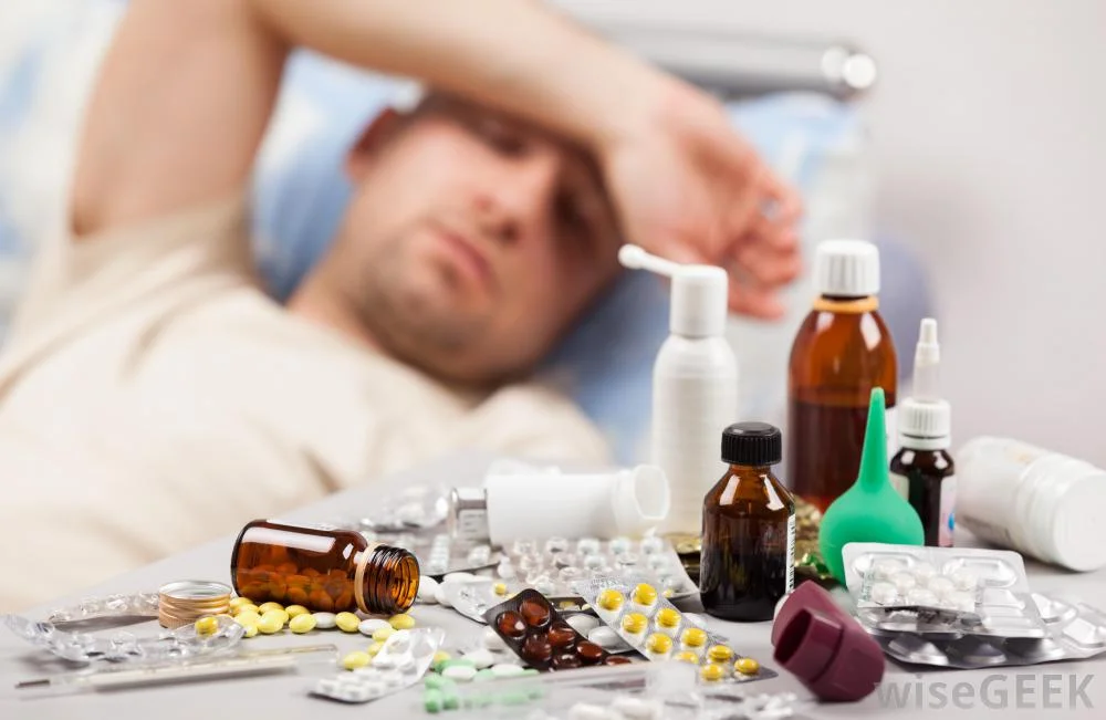 man-with-hand-over-his-head-feeling-ill-in-background-with-close-view-of-pills-and-medicine.jpg