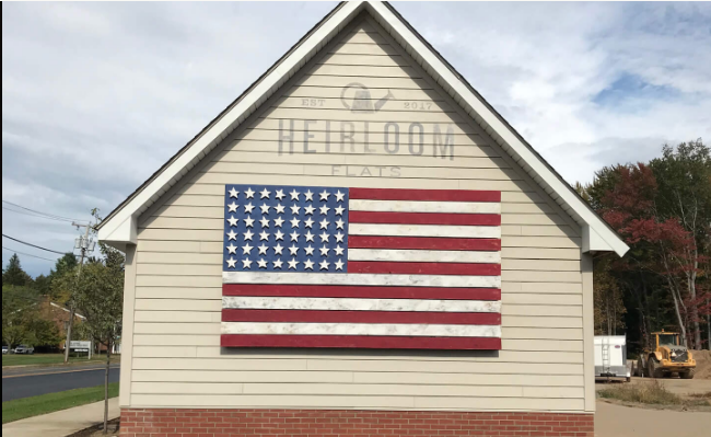Tao created a mixed-media faded American flag and painted logo mural on an exterior wall near the entry to the Heirloom Flats apartment complex project. The artwork is reminiscent of folk art tradition of painting flags on the sides of barns.
