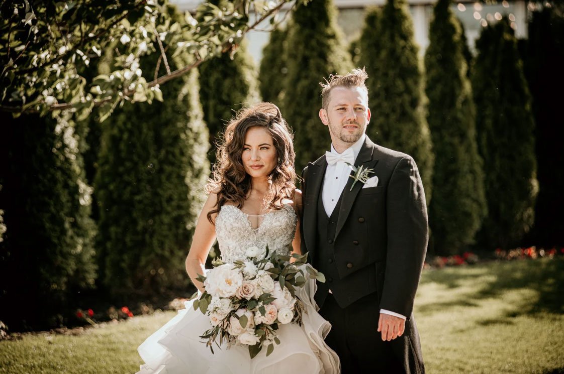 Editorial Style wedding photo of a Bride & Groom looking in different directions but holding each other in the garden at Liberty House in Jersey City, NJ 