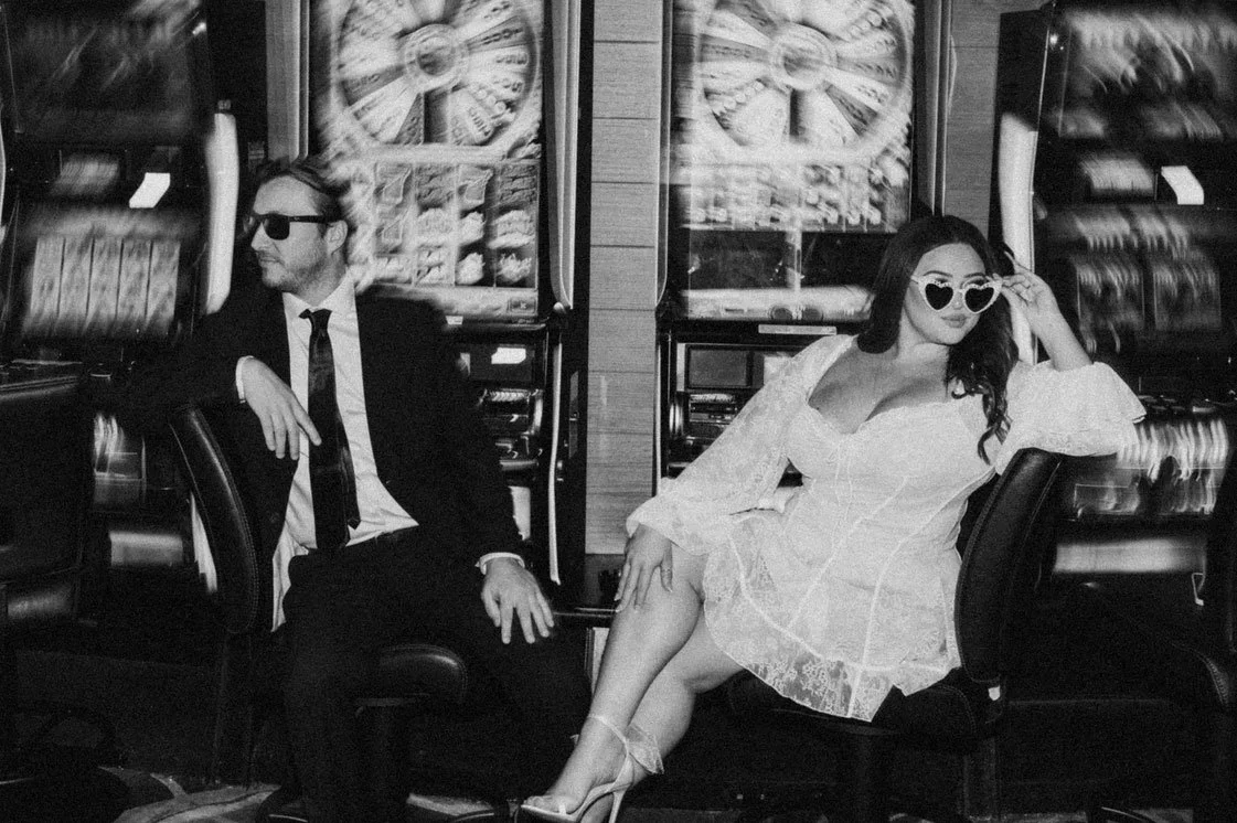 Black & White Atlantic City Ocean's Casino Wedding Photograph of a Bride & Groom wearing sunglasses sitting down with slot machines behind them. 