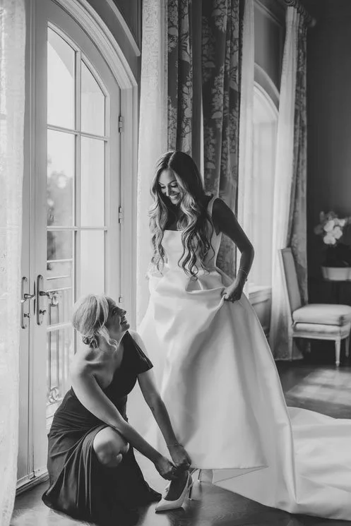 NJ Wedding Film Photographer captured a Bridesmaid helping the Bride put on her shoes at the Park Château Estate bridal suite