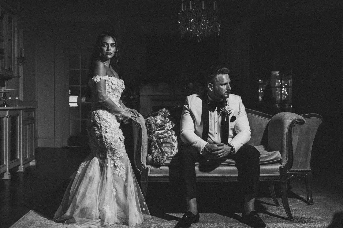 Moody black & white editorial wedding photo of a bride standing while the groom is sitting on a fancy chase couch at Park Savoy in Florham Park, NJ 