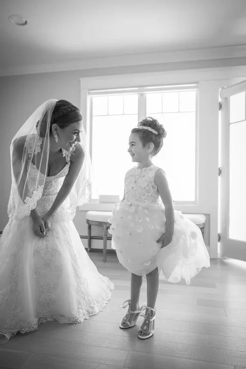 A bride is captured sharing a moment with her flower girl in a black & white wedding photo at Clark's Landing. 