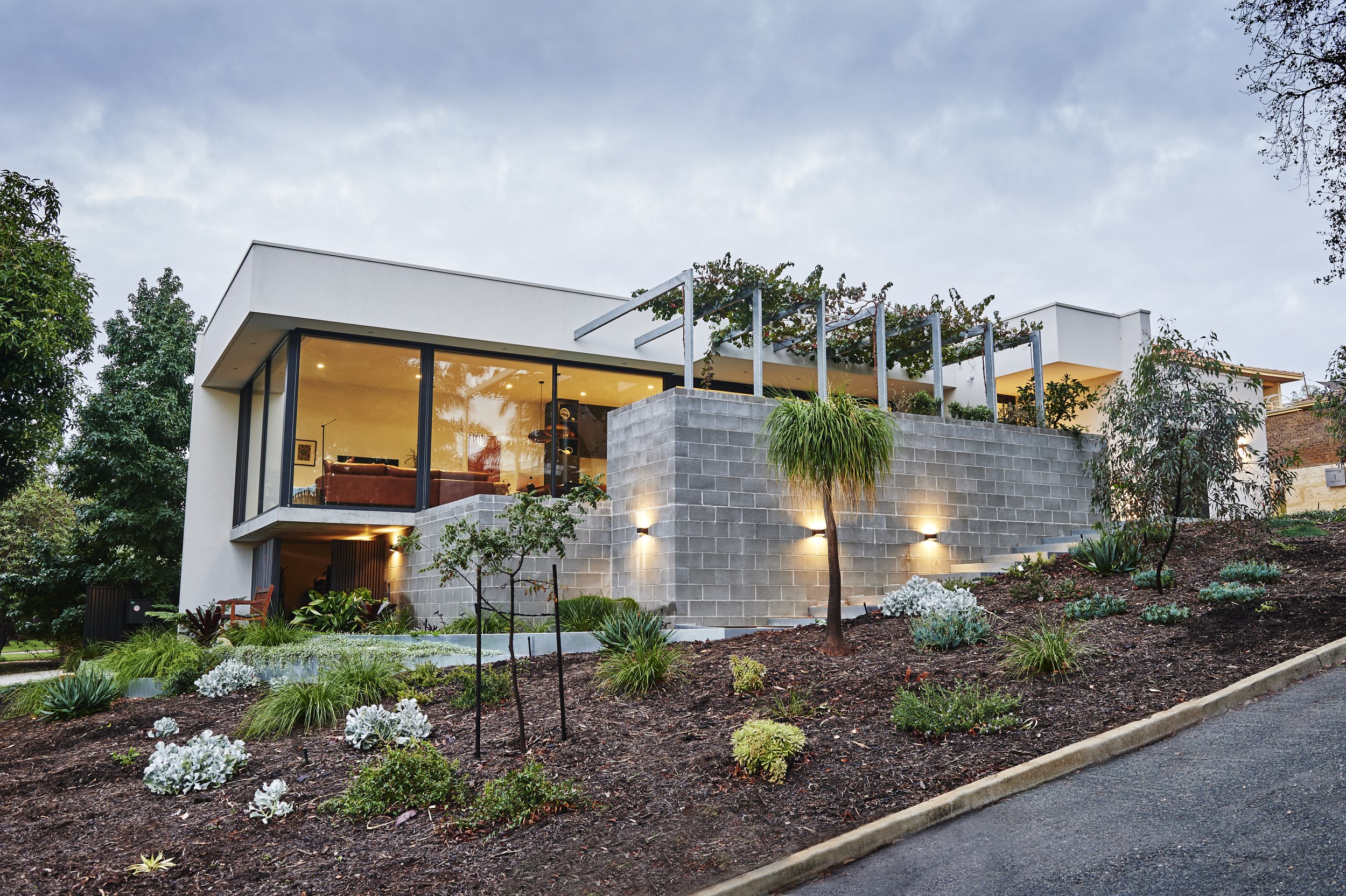 A street view of a custom build with a Pergola covered in vines.
