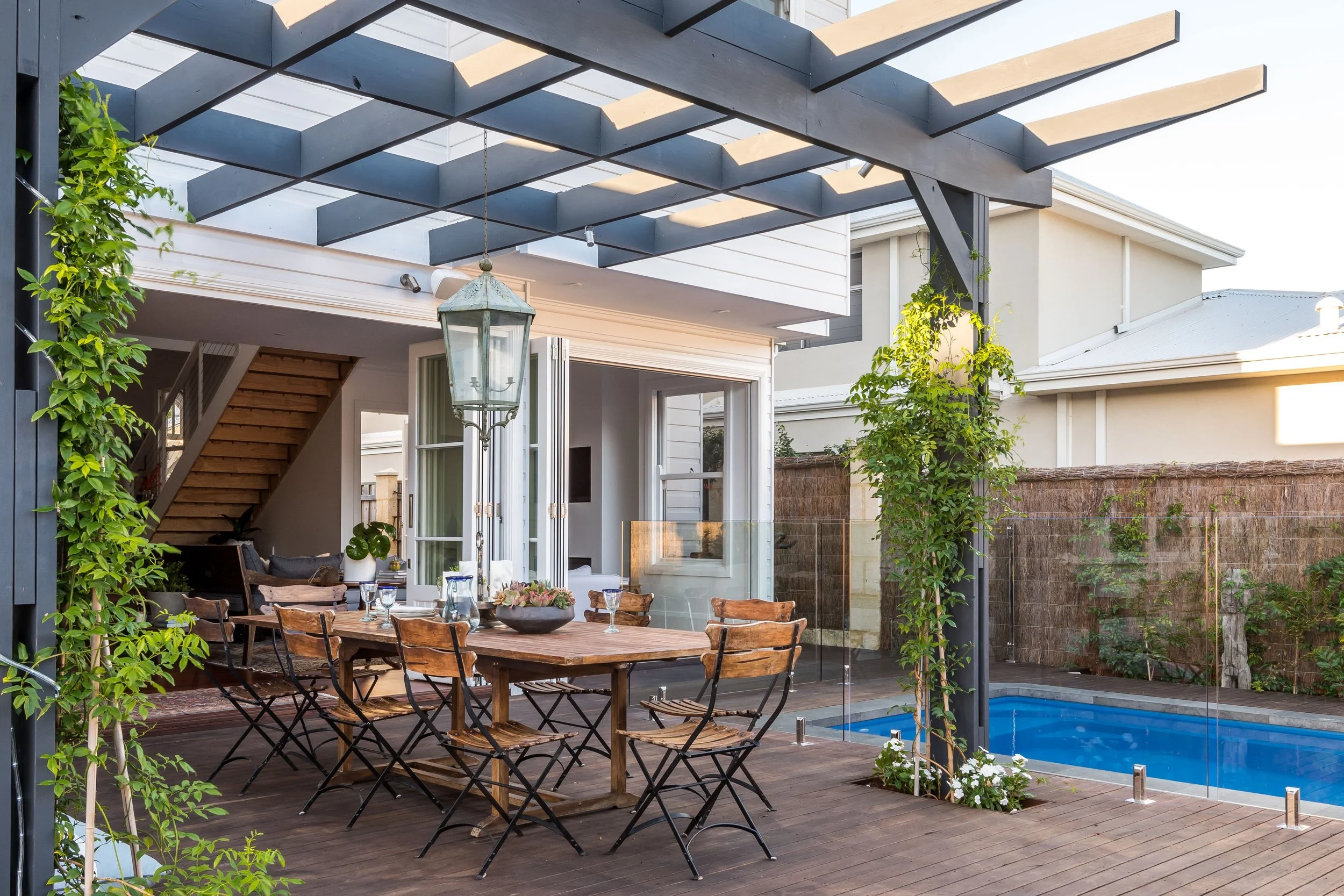 An alfresco with an outdoor dining table, with bifold doors leading into a custom-built house.