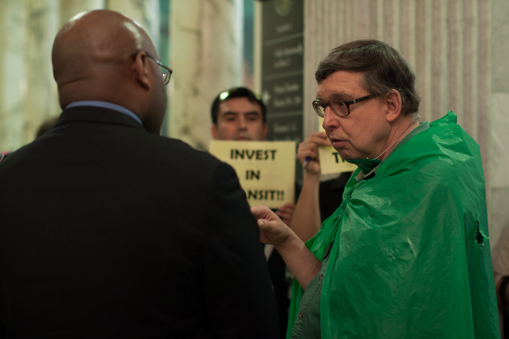 two men talking with a people holding invest in transit signs