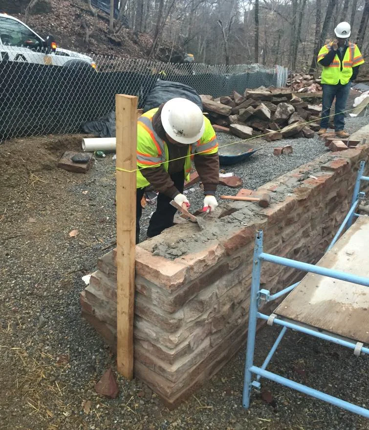  A mason applies mortar between salvaged stones.