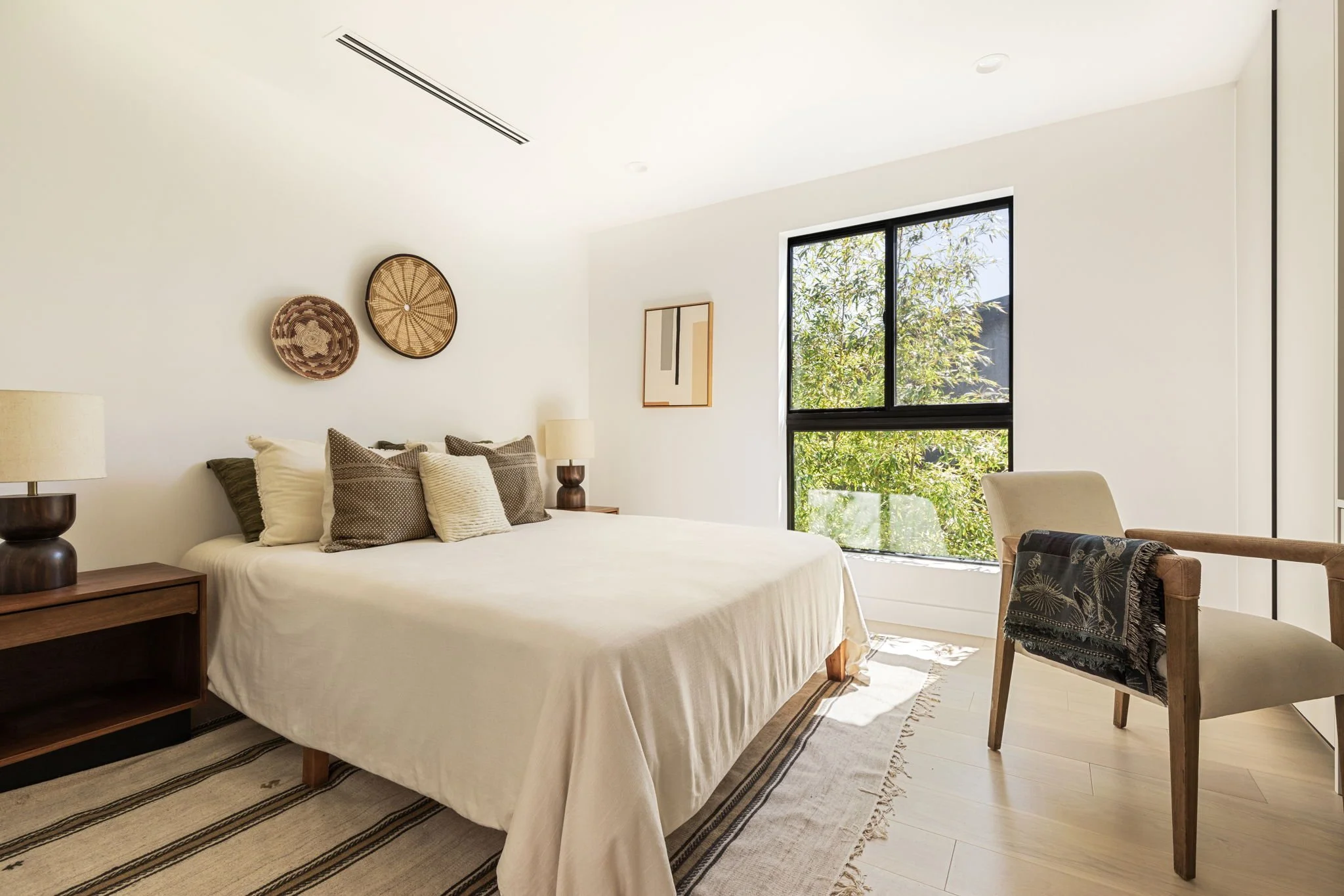  Bedroom with neutral bedding, textured throw pillows and two wooden bedside tables with matching lamps.  