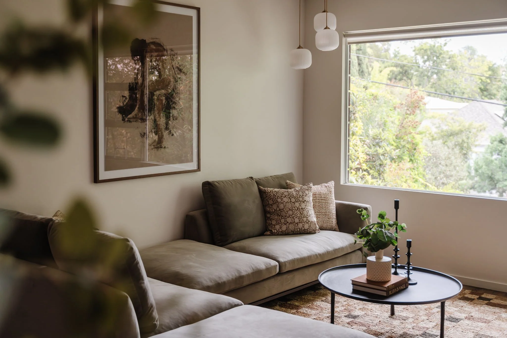  Neutral checkered rug with a sage green velvet couch, round iron-look coffee table, and portrait of a woman.  