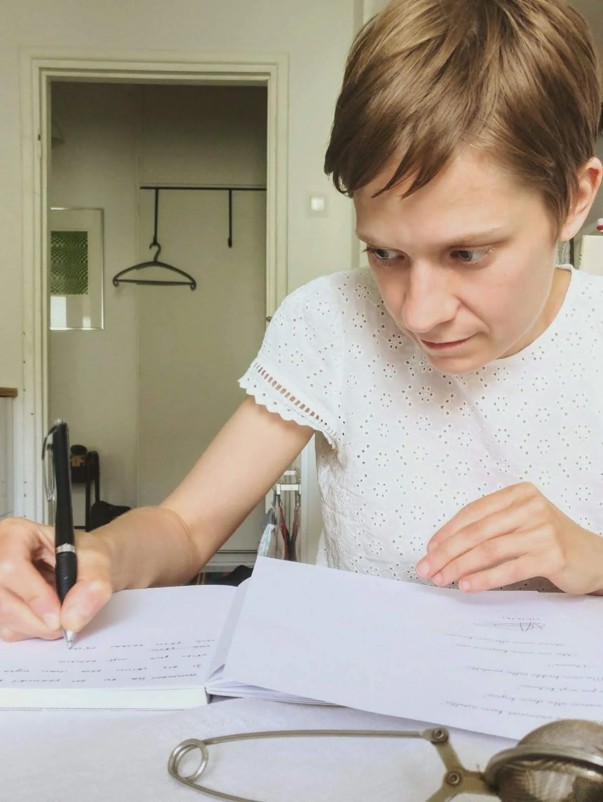 Liisa teekupposen äärellä kirjoittamassa lauseita vihkoon, jonka hankin tätä työtä varten.