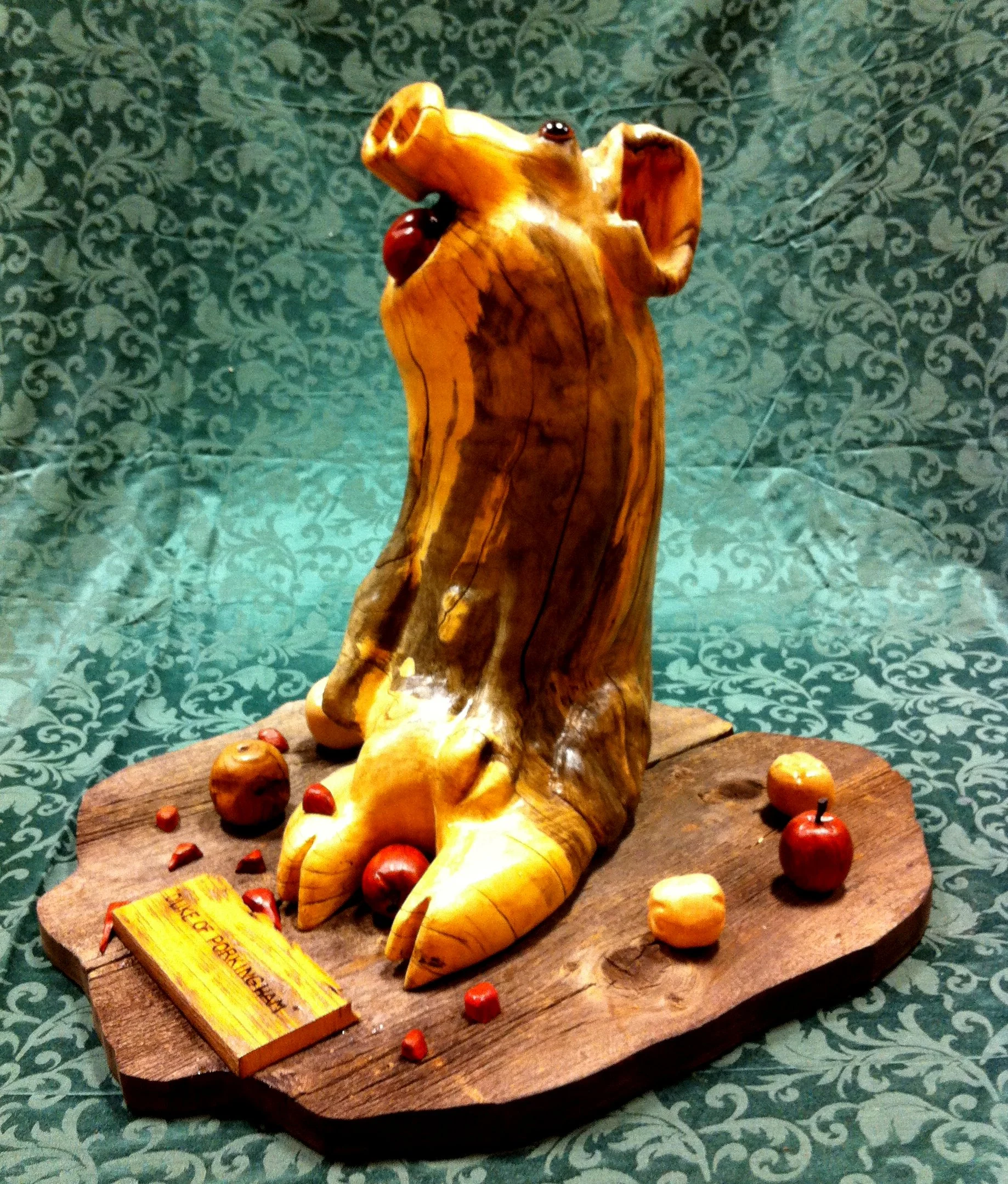 The wood is Box Elder, also called “Manitoba Maple”. The colours of wood you see are all natural, I only put on a coat of clear finish. I left the grey on him to represent that he is sitting in the mud. The “mud” he is sitting on is good, old barn boards. The apples are also carved in natural wood. The red apples, including the one in his mouth, are carved from a wood called “Chakte Kok” or “Redheart” from Brazil. The others are Russian Olive, Butternut and Manzanita, which comes from California.