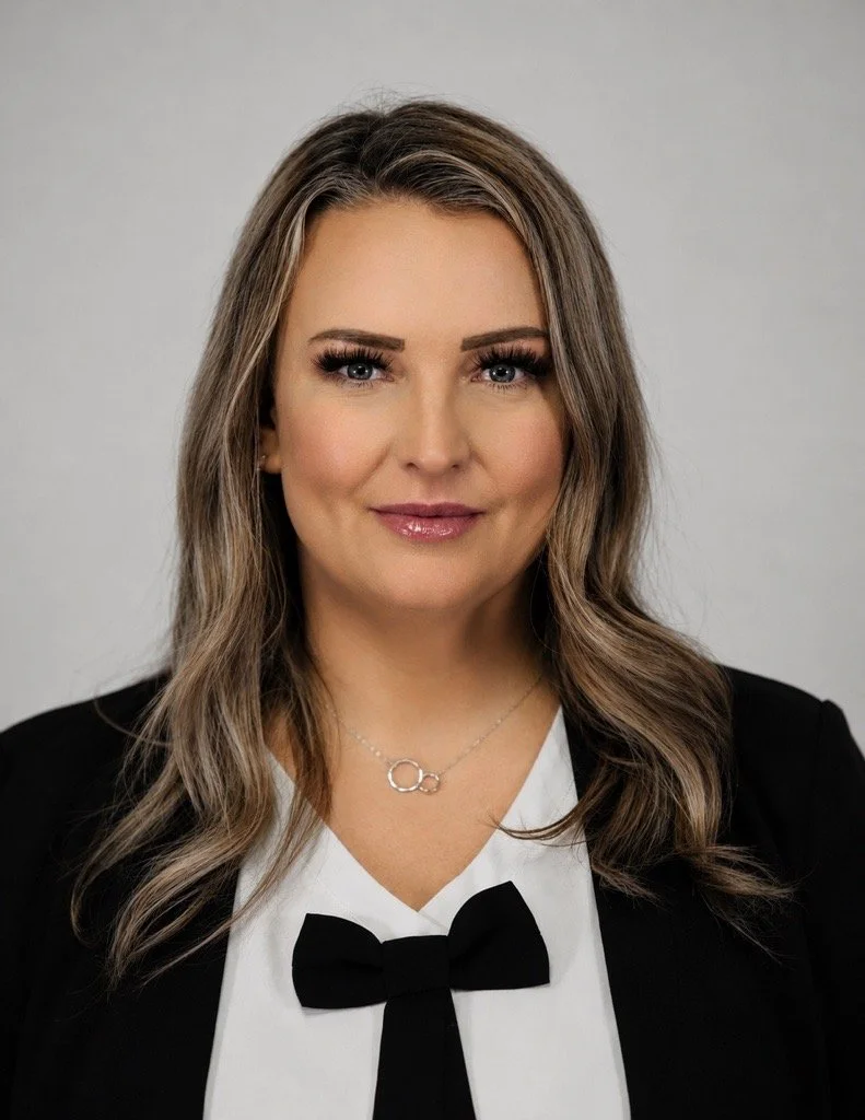Portrait of a woman with straight shoulder-length hair, wearing a black outfit, against a plain background.