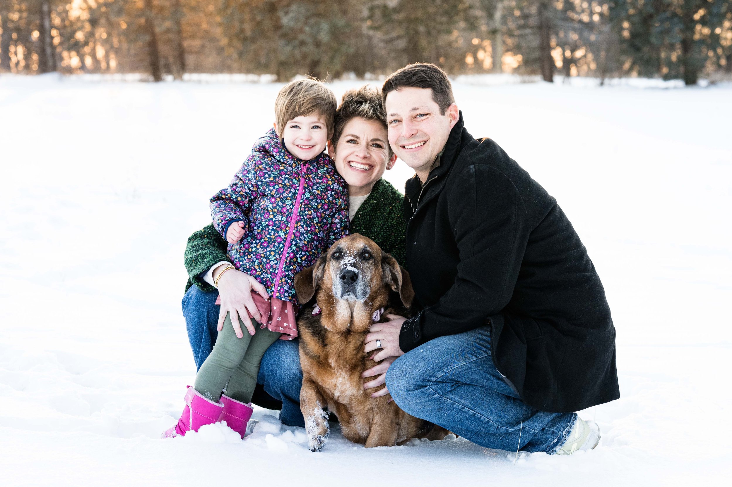 family of three with their basset hound dog in the snow posed for a photo