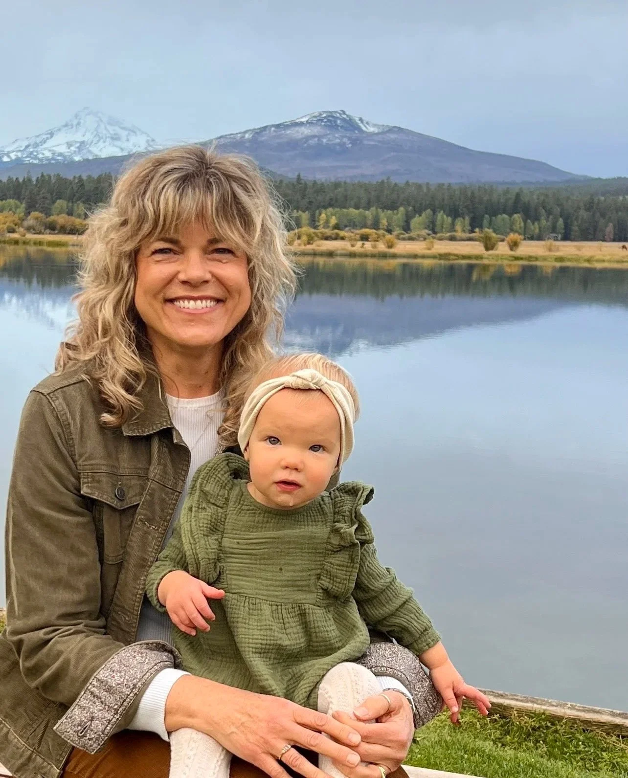women and baby by lake with mountains in the background