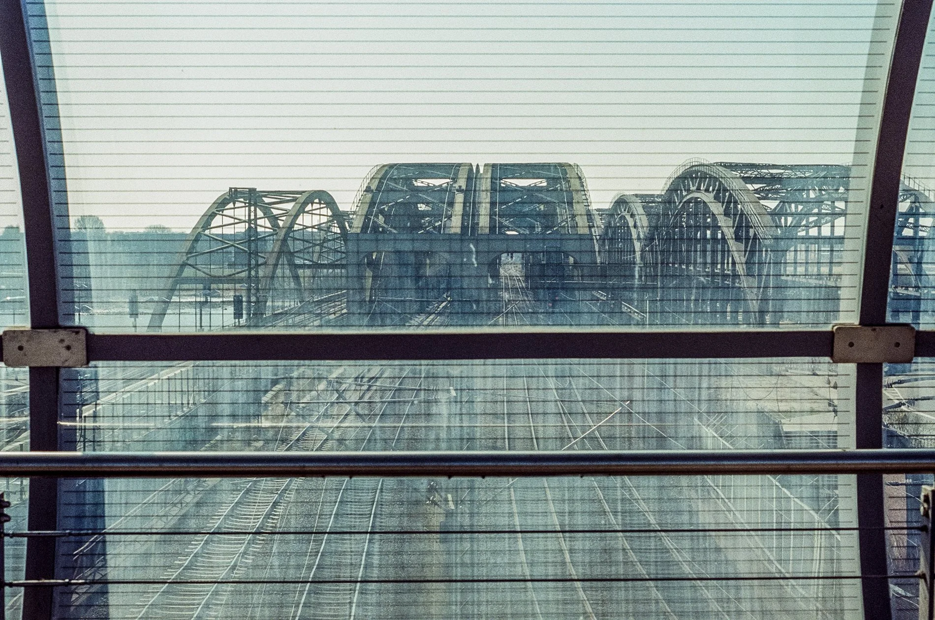 View through a window of a large roller coaster with multiple loops and tracks at an amusement park, seen from inside a building.